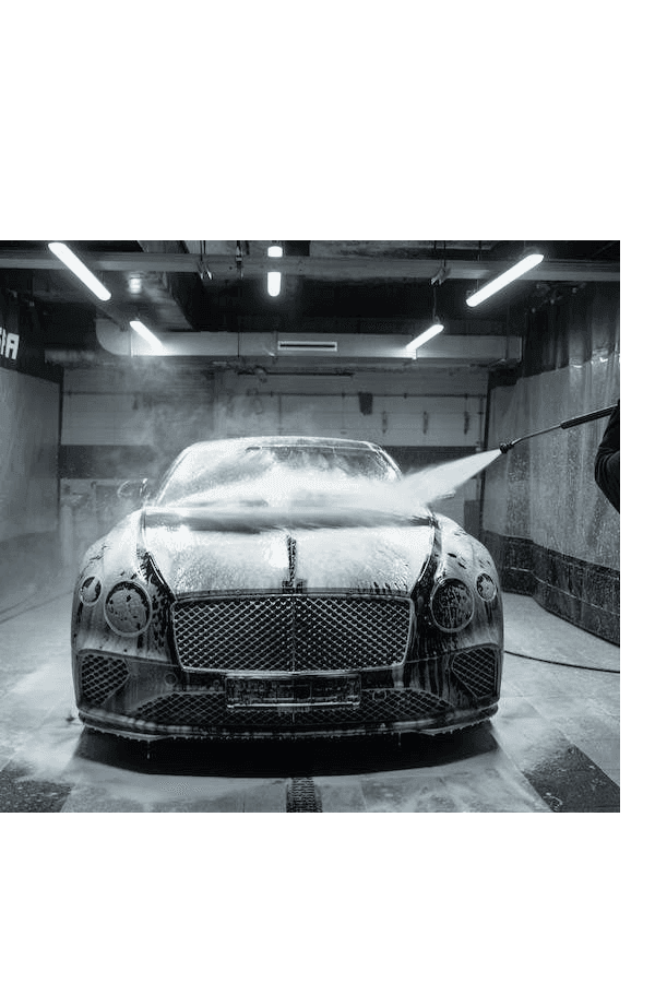 Luxury car being washed with foam and water spray in a car wash station.