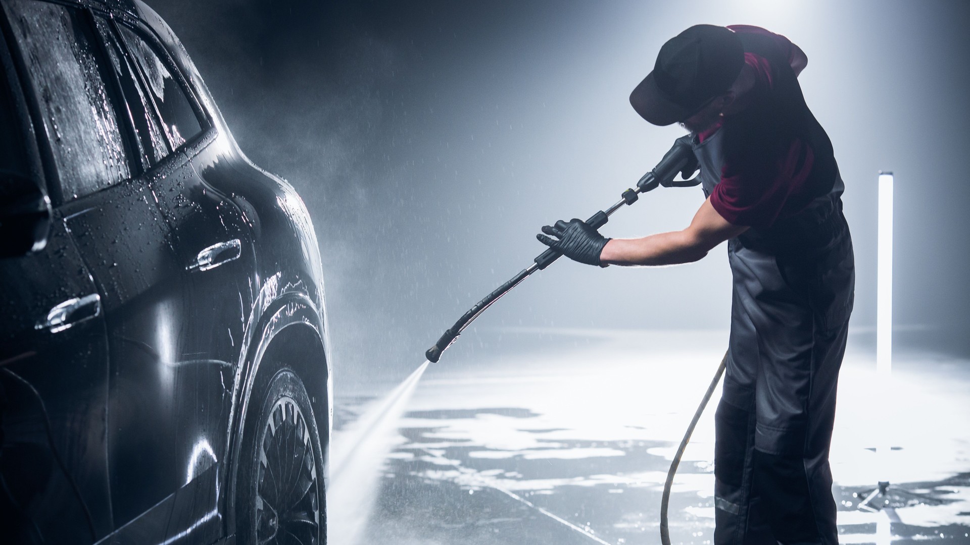 Advertising Style Photo of a Professional Car Wash Specialist Using a High Pressure Washer to Clean and Prepare a High Tech Black Family Electric SUV for Detailing, Polishing and Waxing